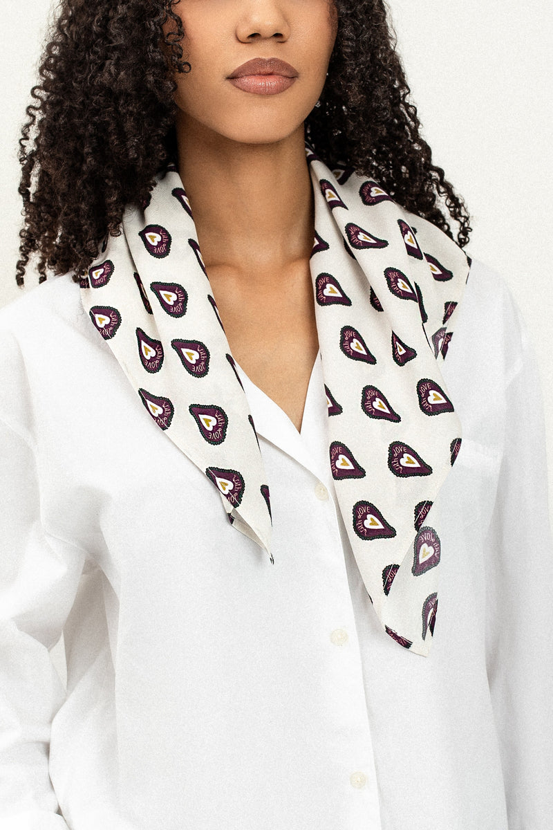 Woman wearing a white blouse with a patterned scarf around her neck against a white background
