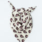 A light-colored scarf tied into a knot and laid against a clean white background. The accessory features a repeating heart pattern: each heart is yellow, encased in a dark burgundy outline with the words "With LOVE." The scarf is arranged in a triangular shape, highlighting the fabric's lightness and the pattern's details.