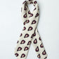 a square, light-colored fabric scarf, artfully folded into a narrow, long strip and looped. It is laid against a clean white background. The accessory features a repeating pattern of dark burgundy shapes, each with a yellow heart and the text "With LOVE" inside.