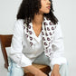 Woman wearing a white shirt with a patterned viscose scarf, sitting on a chair against a plain background