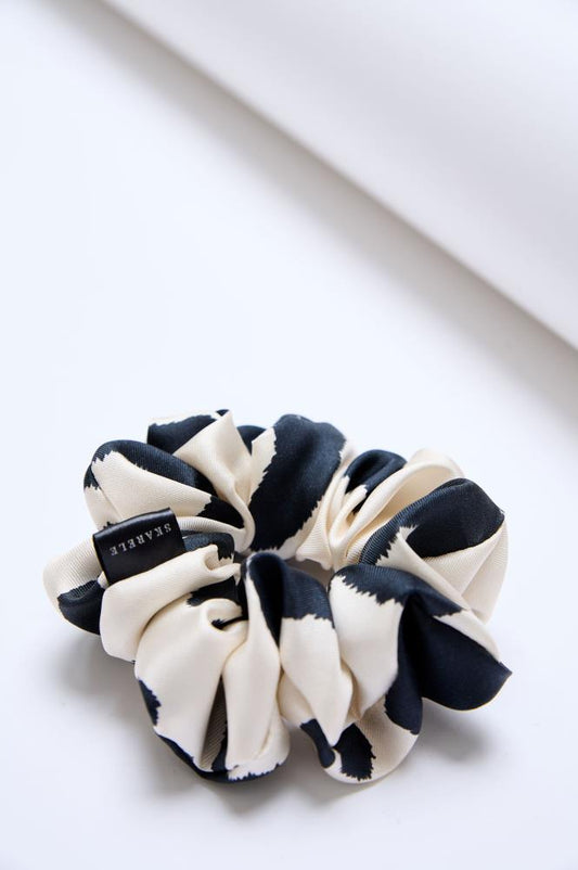 Close up of A mid-size black and white silk scrunchie on a light background.