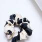 Close up of A mid-size black and white silk scrunchie on a light background.