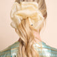 Woman with long blonde hair wearing a large champagne hue silk organza scrunchie on a beige background