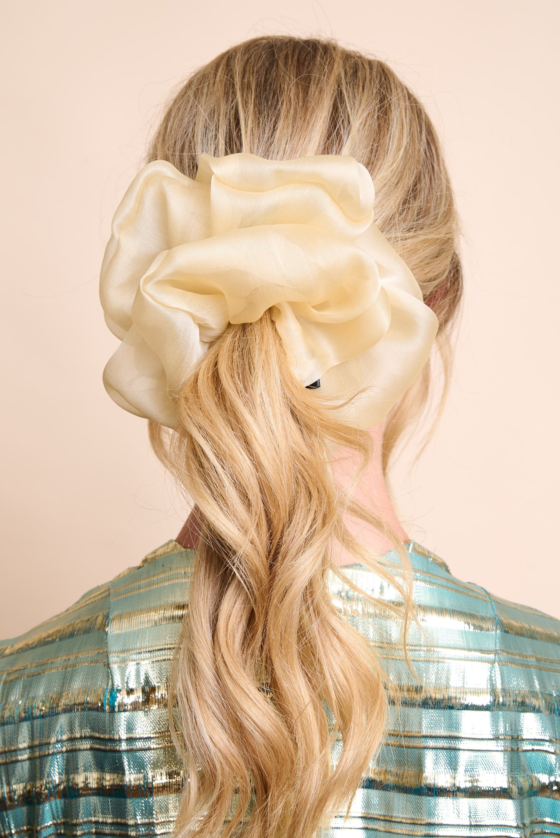 Woman with long blonde hair wearing a large champagne hue silk organza scrunchie on a beige background