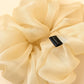 Cream-colored silk organza scrunchie with a brand label on a light yellow background