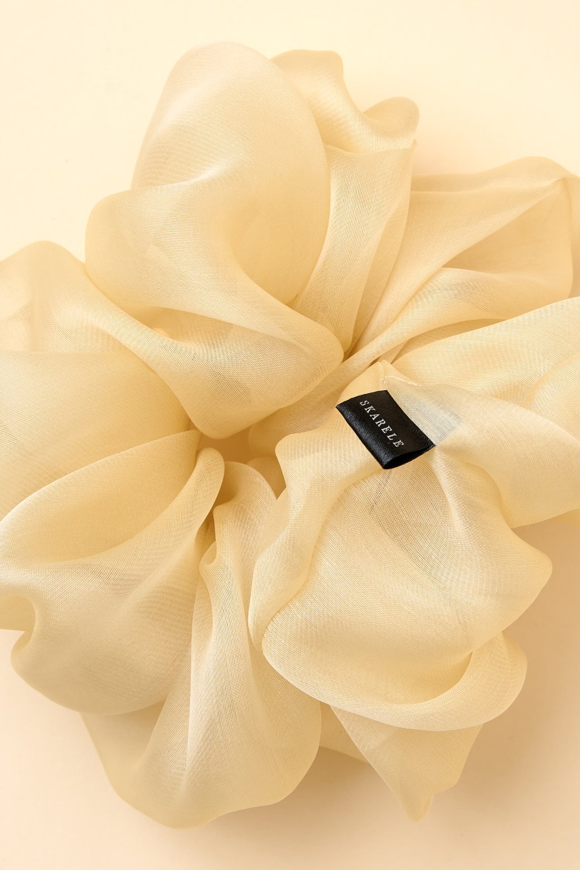 Cream-colored silk organza scrunchie with a brand label on a light yellow background