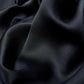 A crumpled black silk scarf with a matte side and a satin-shiny side, providing a textured background.