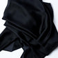Top-down view of a large black silk shawl arranged in loose, voluminous drapes against a bright white background. The contrast between the dark material and the clean surface highlights the smooth texture and fine edges of the fabric.