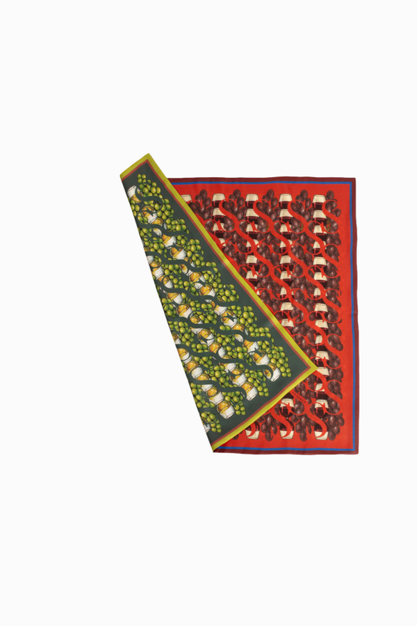 A top-down view of a double-sided silk scarf displayed flat on a white background. One side features a green grape pattern on a dark base, and the other side shows a red wine-themed print.