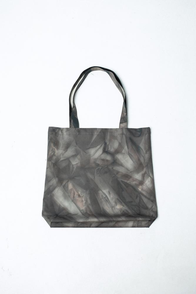 A front view of a fabric tote bag featuring an abstract, smoky geometric pattern in charcoal grey and pale reddish-brown tones, displayed against a white background.