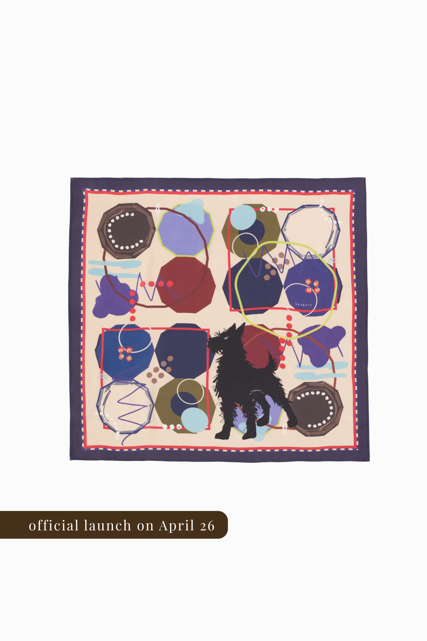 A square silk scarf featuring a full abstract print with a central black dog silhouette. The design consists of various geometric shapes, circles, and scribbles in navy, burgundy, and olive green on a cream background. A thin red and white dotted border frames the artwork. Below, a brown banner indicates the official launch on April 26.