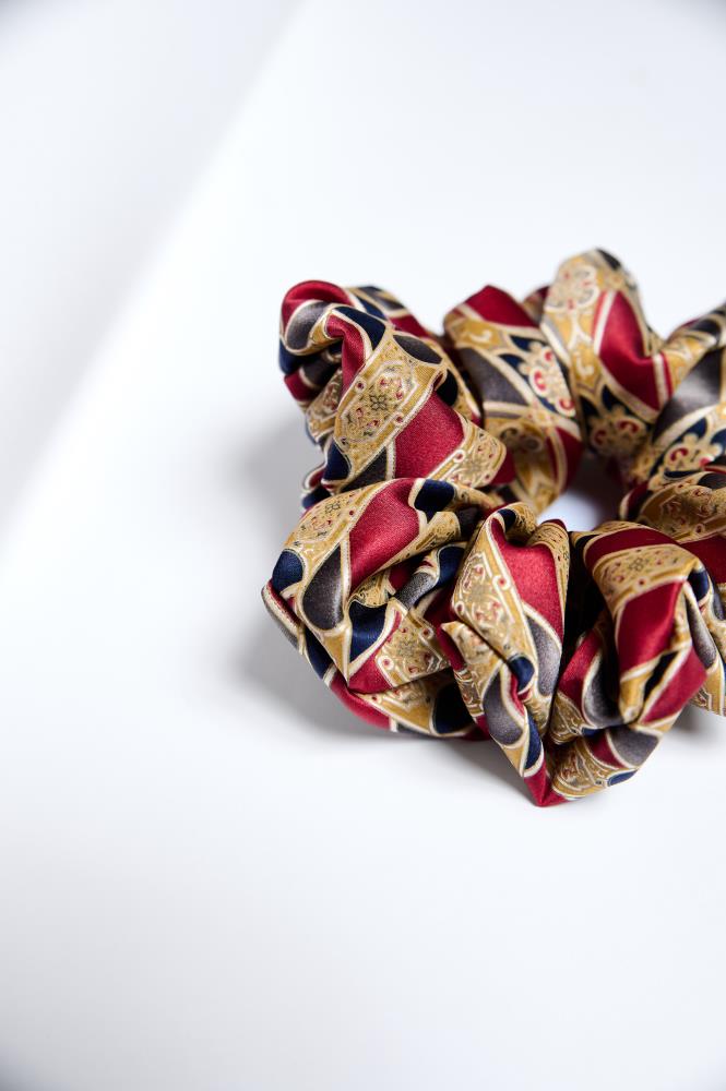 A mid-size silk scrunchie with a geometric pattern in shades of red, gold, grey, and blue.