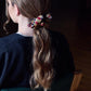 A person with long hair has their back turned to the camera, wearing a silk scrunchie in her hair. The scrunchie is visible and have a geometric pattern.
