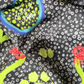 Macro close-up of draped Skarele La Dolce Vita viscose & silk blend scarf. Shows premium satin texture, white dotted print on dark greyish-brown fabric, lime green wavy lines, crabs, and lemon illustrations.