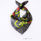 Product shot of a large 70x70 cm luxury viscose & silk blend blend scarf folded in a loose loop. Highlights the draped greyish-brown satin texture with a playful summer crab and lemon motif on a white backdrop.