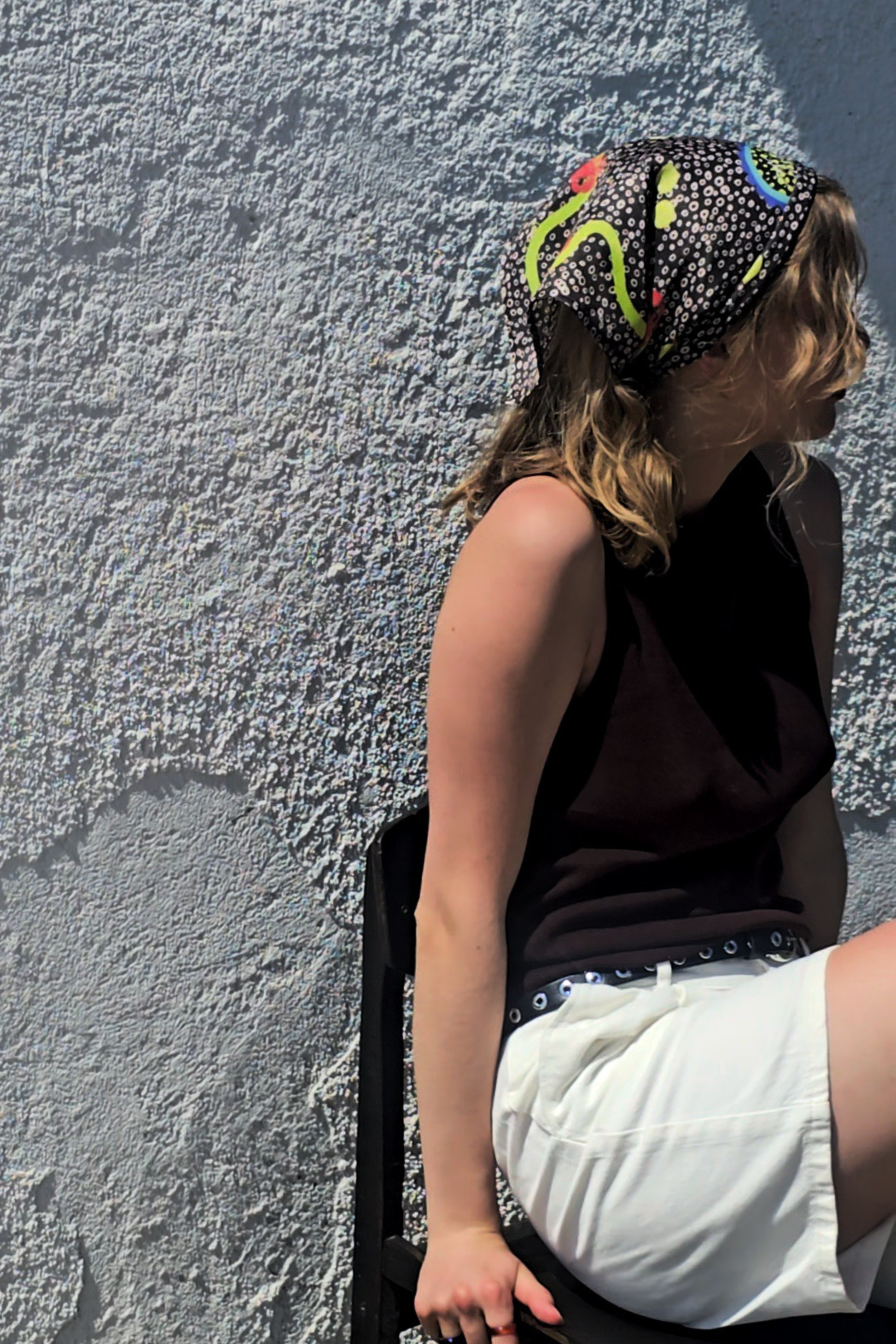 Woman styling the dark greyish-brown La Dolce Vita silk bandana on her head. Summer lifestyle fashion shot showcasing a luxury patterned headscarf on a sunny day.