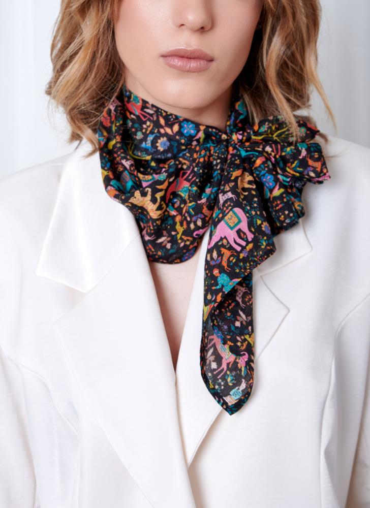 A woman wearing a white blazer with a multicolored, intricately patterned silk scarf tied in a bow at the neck. The image conveys elegance and style.