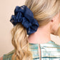 Navy blue silk organza scrunchie in a blonde ponytail against a beige background