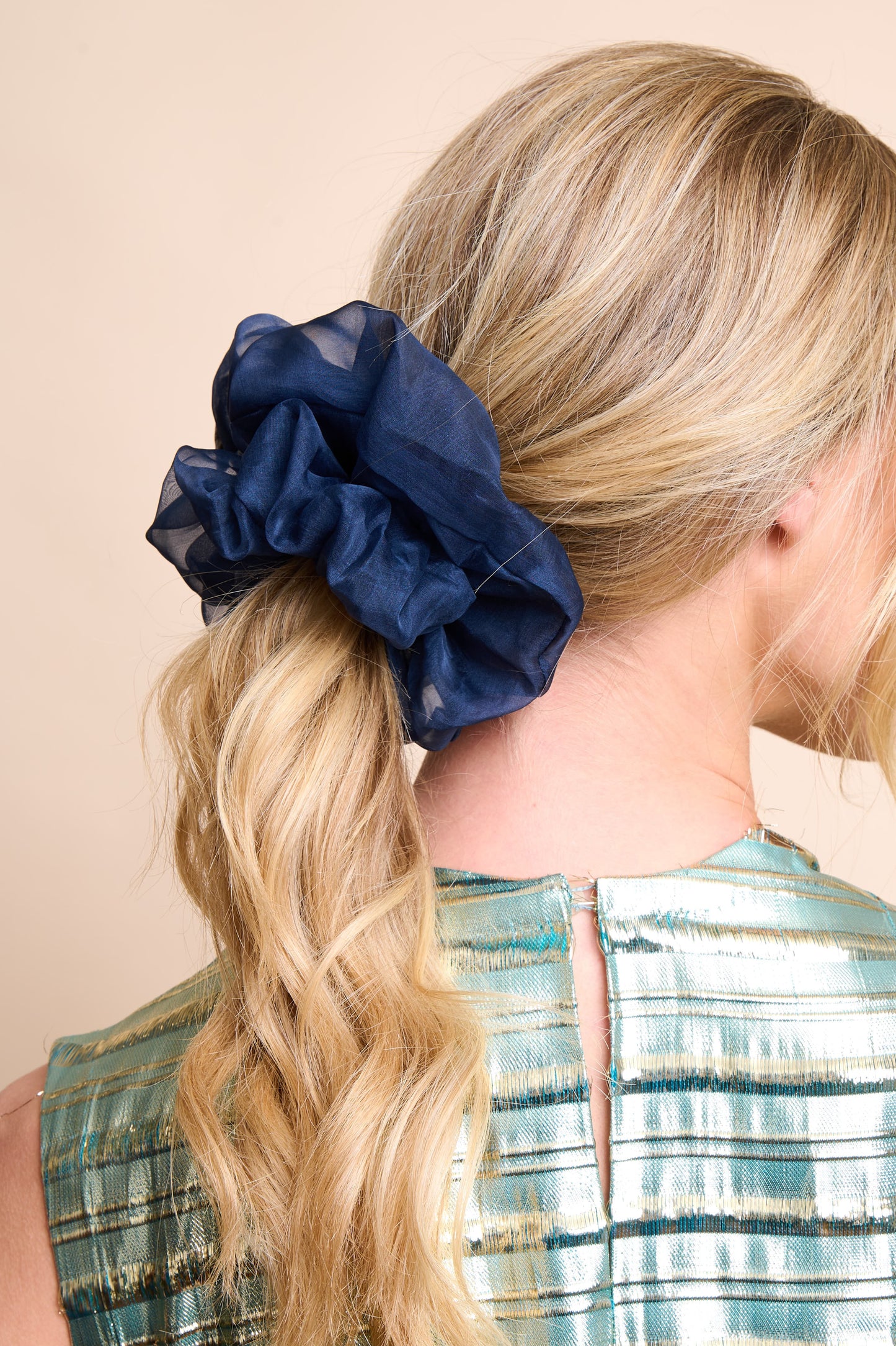 Navy blue silk organza scrunchie in a blonde ponytail against a beige background