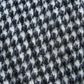 an extreme close-up of a wool fabric texture featuring a classic houndstooth pattern. The photo clearly shows the dense weave and the natural fuzziness of the material. The contrast between black and white creates a dynamic, graphic look that emphasizes the high quality of the product and the coziness of the fabric.