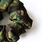 A detailed close-up of a luxury patterned silk scrunchie, showcasing vibrant green leaf motifs and rich brown details on the fabric folds