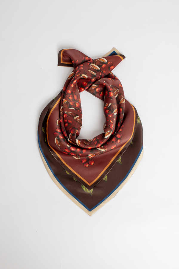 A luxury square silk scarf with a deep brown and terracotta gradient. Features a pattern of coffee beans, coffee cherries, and leaves. Styled on a white background.
