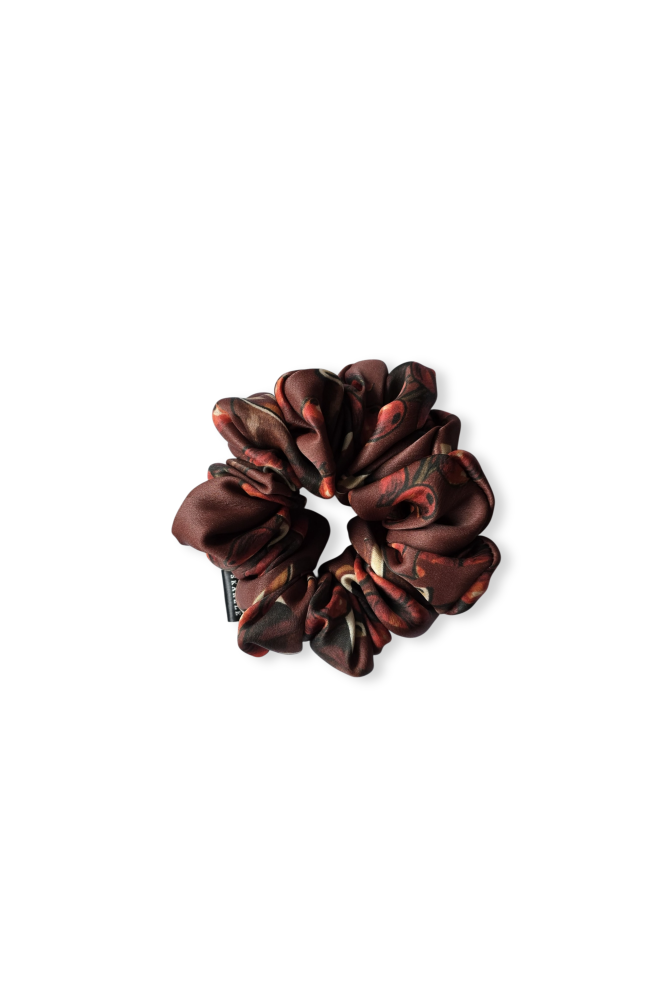 Top-down view of a silk hair scrunchie with an elegant brown and burnt orange abstract floral pattern on a pure white background.