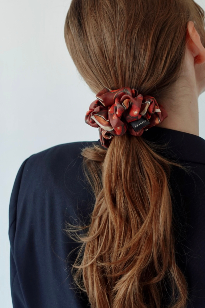 Rear view of a person with light brown hair in a ponytail, styled with a brown and burnt orange silk scrunchie, wearing a dark navy blue blazer.