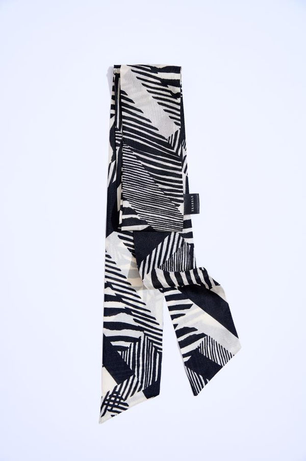 A black and white silk twilly scarf with a geometric pattern, displayed in a twisted arrangement on a plain background.