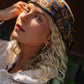 radiant blonde woman basks in the sun, wearing a vibrant patterned bohemian silk headscarf and a cozy crocheted top, evoking a carefree, summery vibe.