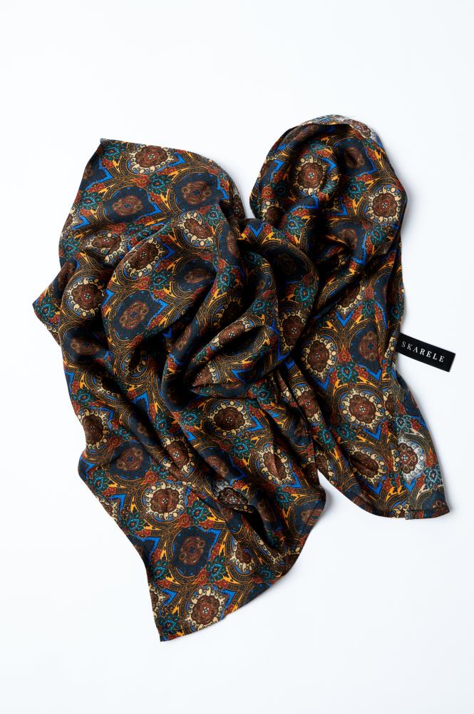 A patterned silk scarf with colors predominantly in brown and black, displayed in a crumpled manner on a white background with a tag visible.