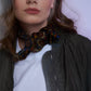 Close-up of a woman wearing an olive green bomber jacket and a white tee, styled with a knotted paisley silk scarf for a sophisticated urban look.