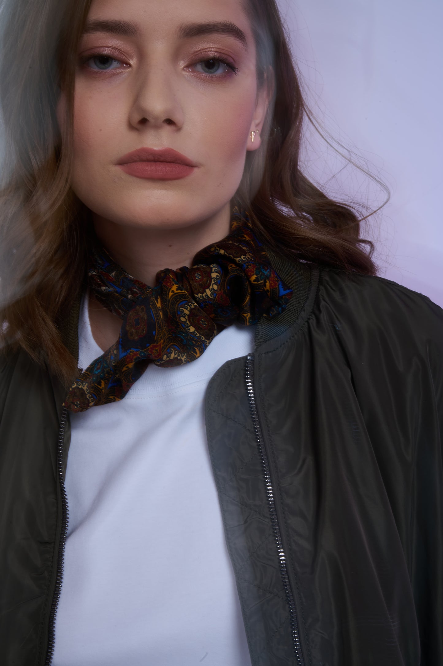 Close-up of a woman wearing an olive green bomber jacket and a white tee, styled with a knotted paisley silk scarf for a sophisticated urban look.