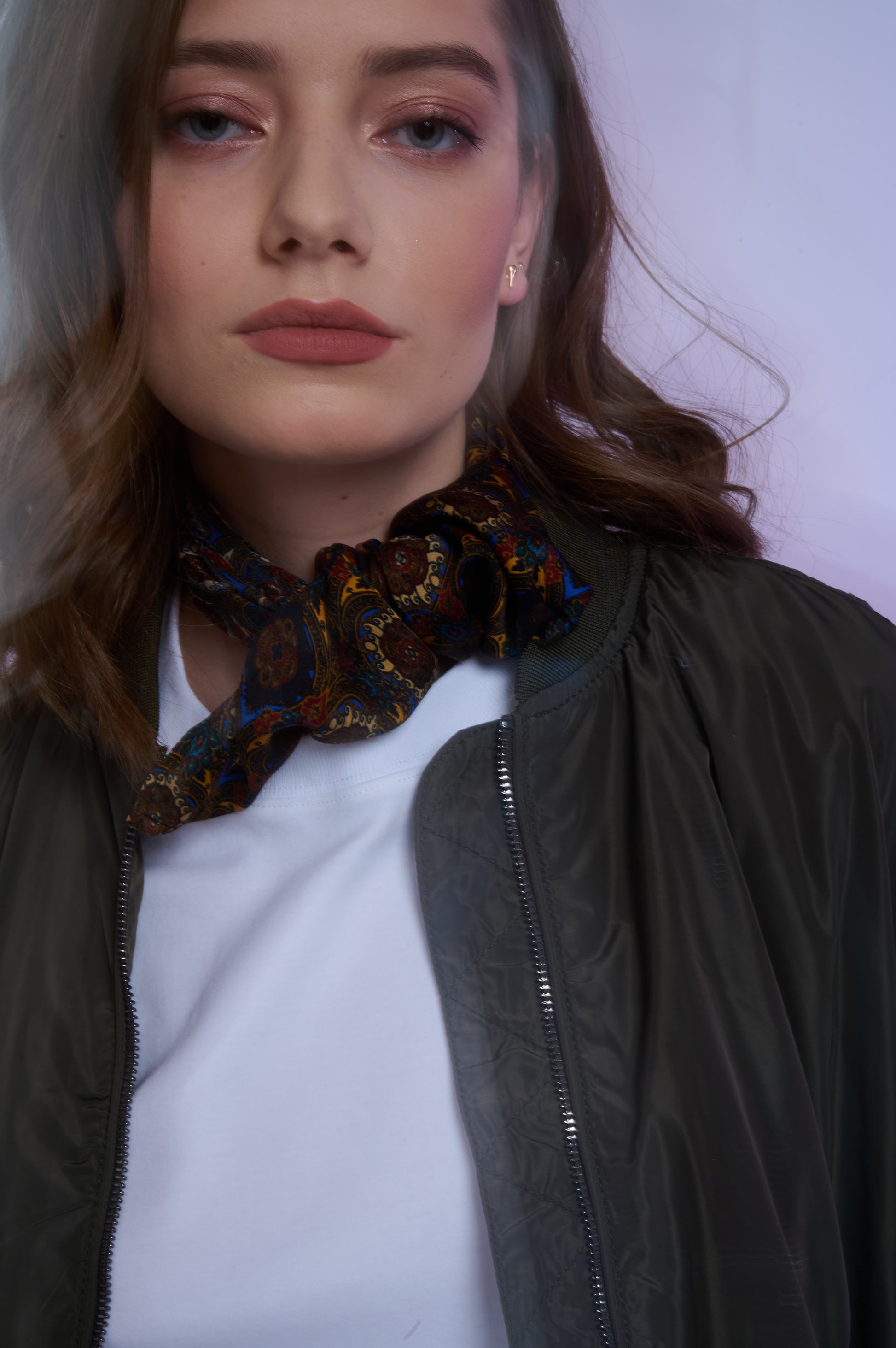 Close-up of a woman wearing an olive green bomber jacket and a white tee, styled with a knotted paisley silk scarf for a sophisticated urban look.