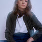Artistic, moody portrait of a model with a blurred motion effect, wearing a knotted paisley silk scarf, olive bomber jacket, and jeans for a cool, urban aesthetic.