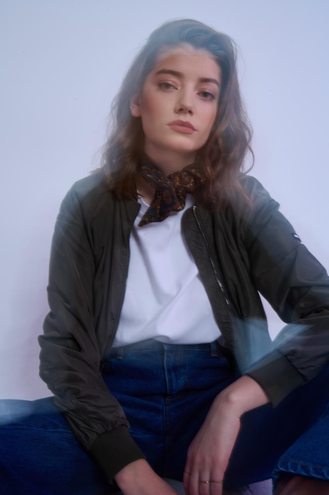 Artistic, moody portrait of a model with a blurred motion effect, wearing a knotted paisley silk scarf, olive bomber jacket, and jeans for a cool, urban aesthetic.