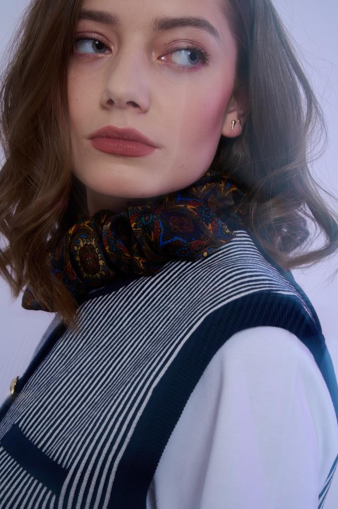 Close-up portrait of a model featuring an intricately patterned silk neck scarf paired with a striped vest, creating a sophisticated and layered high-fashion look.
