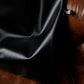 A close-up of a premium black eco leather tote bag, focusing on the soft texture and elegant folds, featuring the "SKARELE" brand label against a rich brown leather armchair.