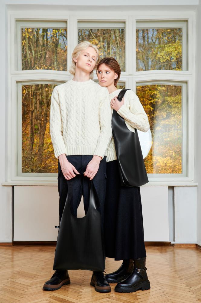 A man and a woman posing together with large black eco-leather tote bags, showcasing the product's unisex appeal and minimalist design in a stylish indoor setting.