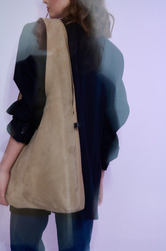 Artistic, blurred motion shot of a model wearing a slouchy tan suede tote bag, capturing a dreamy and modern fashion aesthetic.