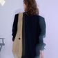 Minimalist studio shot of a model from behind, featuring a spacious beige suede tote bag draped over a black blazer, evoking a clean and sophisticated urban vibe.