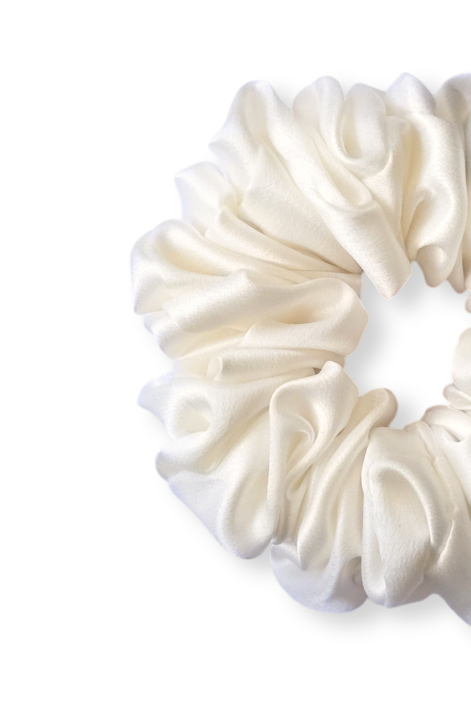 close up view of a luxury, white gathered silk scrunchie, displayed flat against a clean white background. It features a soft, lustrous texture