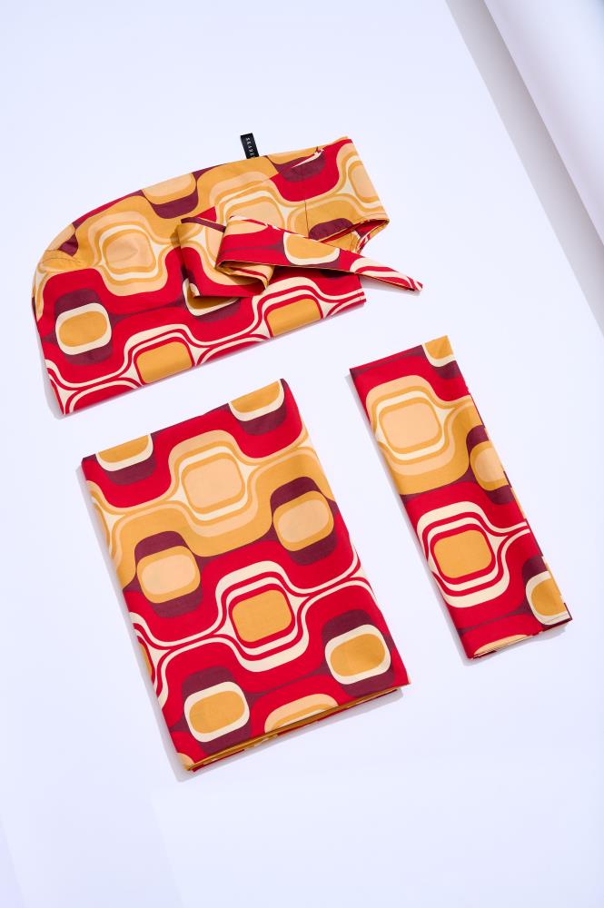 A set of three pieces of clothing with a retro geometric pattern in red, golden, and burgundy tones, including a scarf, a beach/picnic blanket, and a tote bag.