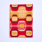 A rectangular folded piece of fabric placed vertically against a clean white background. The material features a bold retro-style pattern consisting of wavy lines and rounded squares in yellow, orange, red, and burgundy.