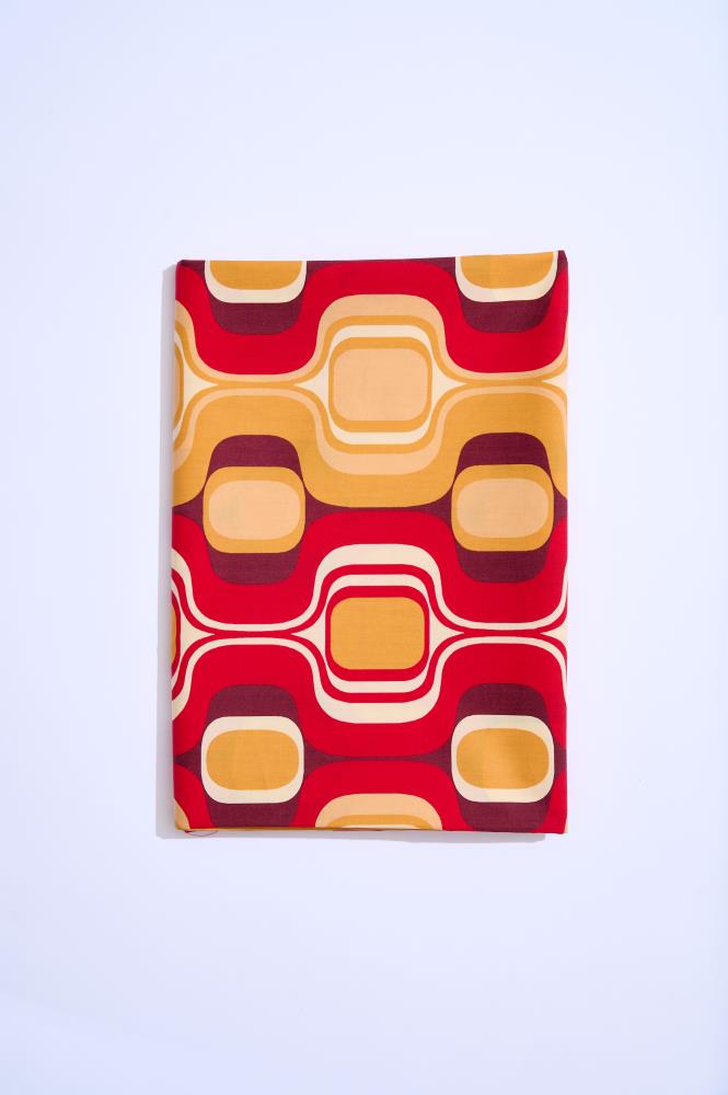 A rectangular folded piece of fabric placed vertically against a clean white background. The material features a bold retro-style pattern consisting of wavy lines and rounded squares in yellow, orange, red, and burgundy.