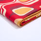A close-up of folded fabric against a clean white background. The material features a bold retro-style pattern with rounded squares in yellow, orange, red, and burgundy. This detailed shot highlights the texture and the richness of the fabric's design.