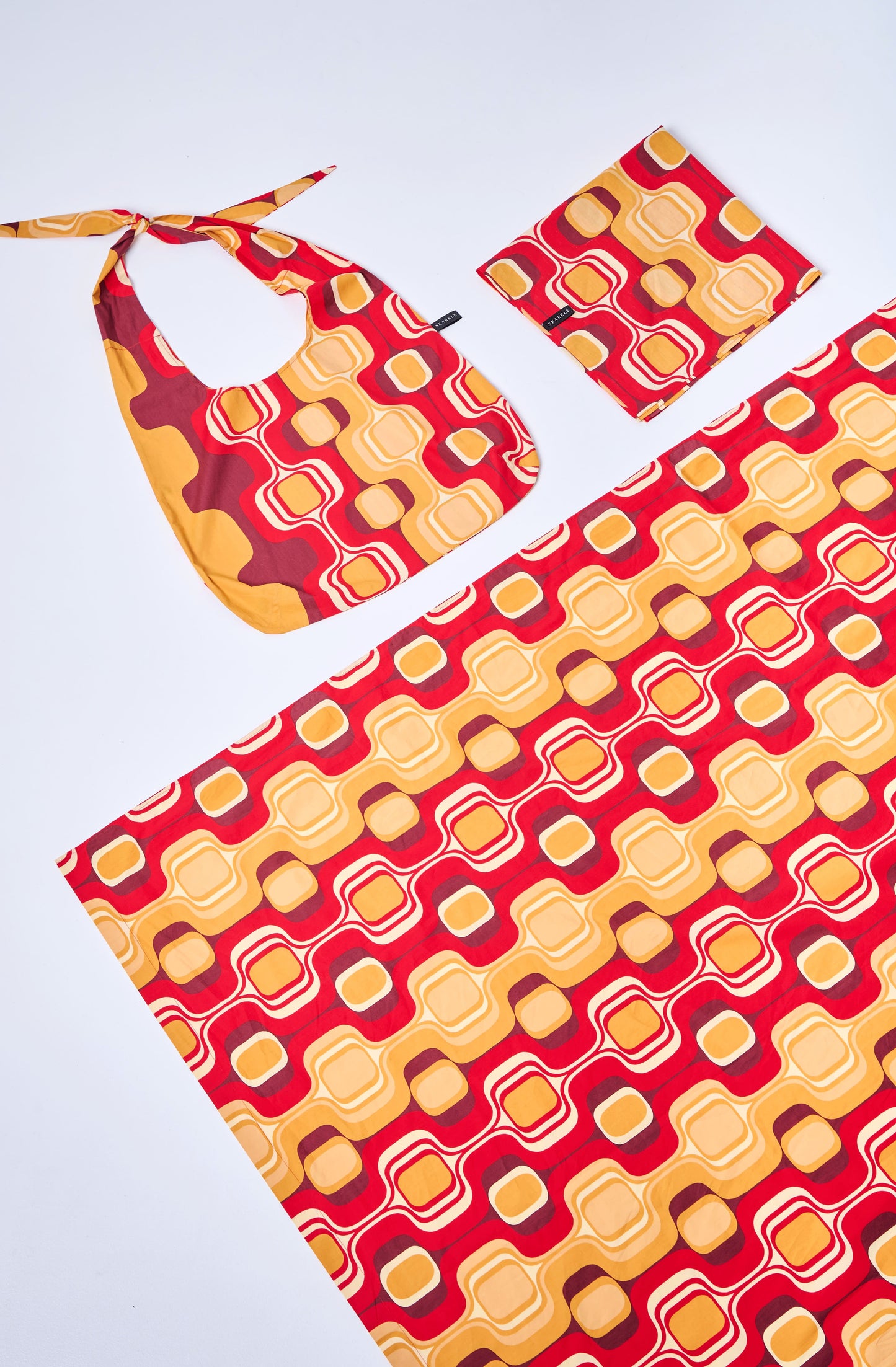Set of red and yellow patterned blanket, scarf, and tote bag on a white background