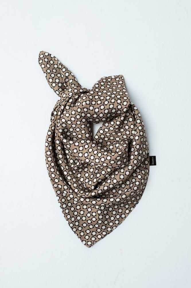 A flat lay view of a draped viscose scarf featuring a brown, black, and white geometric retro pattern against a clean white background. Shows a small black logo tag.
