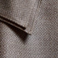 A close-up of a dark grey or brown fabric with a fine, repeating diamond-shaped geometric pattern. The photo shows the corner of a scarf or shawl and the stitching along the edge. The fabric's texture appears soft and dense, while the pattern adds subtle depth and elegance to the material.