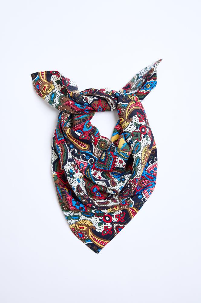 A colorful patterned scarf tied into a knot and laid against a clean white background. The accessory features a rich paisley and botanical pattern, combining vibrant blue, red, yellow, green, and black colors. The scarf is arranged in a triangular shape, highlighting the fabric's softness and the intensity of the colors.
